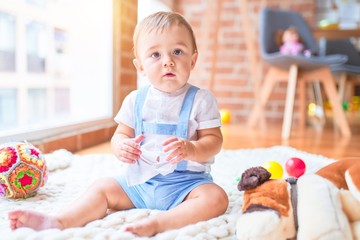 Fototapeta premium Beautiful toddler sitting on the blanket around lots of toys at kindergarten