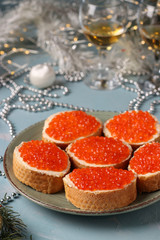 Sandwiches with red caviar are located on a plate against a light blue background, Festive snack, vertical orientation