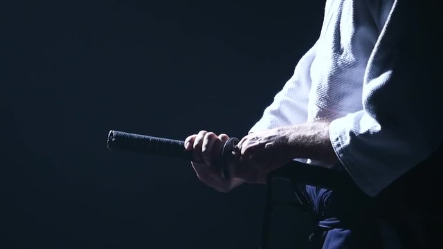 Man fighting at Aikido training with japanese sword katana in martial arts school. Healthy lifestyle and sports concept in the dark studio. Slow motion. Close up.