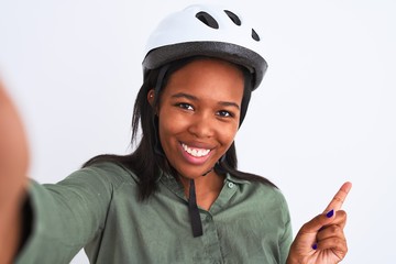Young african american woman wearing bike helmet taking a selfie over isolated background very happy pointing with hand and finger to the side