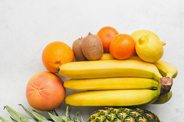 Assortment of tropical fruits, banana, kiwi, orange, tangerine, lemon, pineapple, grapefruit on textured white background, top view