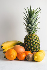 Assortment of tropical fruits, banana, kiwi, orange, tangerine, lemon, pineapple, grapefruit on textured white background