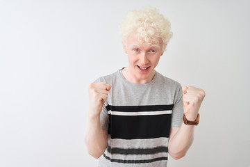 Young albino blond man wearing casual t-shirt standing over isolated white background celebrating surprised and amazed for success with arms raised and open eyes. Winner concept.