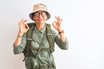 Middle age hiker woman wearing backpack canteen hat glasses over isolated white background relax and smiling with eyes closed doing meditation gesture with fingers. Yoga concept.