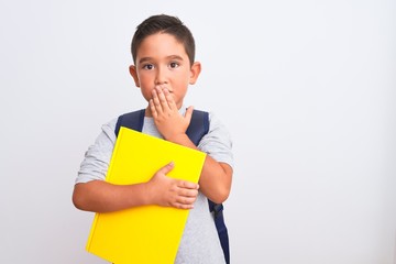 Beautiful student kid boy wearing backpack holding book over isolated white background cover mouth with hand shocked with shame for mistake, expression of fear, scared in silence, secret concept