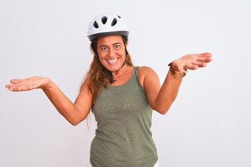 Middle age mature cyclist woman wearing safety helmet over isolated background smiling cheerful offering hands giving assistance and acceptance.