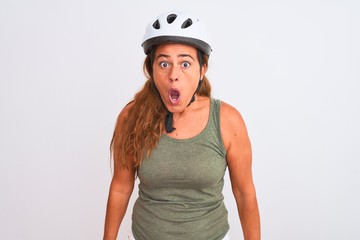 Middle age mature cyclist woman wearing safety helmet over isolated background afraid and shocked with surprise and amazed expression, fear and excited face.