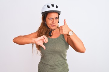 Middle age mature cyclist woman wearing safety helmet over isolated background Doing thumbs up and down, disagreement and agreement expression. Crazy conflict