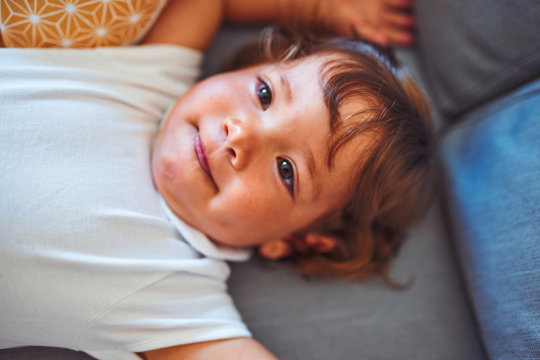Beautiful toddler child girl wearing white bodysuit lying down on the sofa