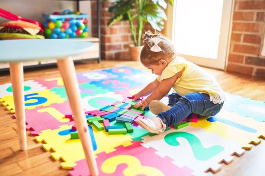 Beautiful toddler sitting on puzzle carpet playing with wooden building blocks at kindergarten