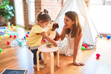 Young beautiful teacher playing with dog doll and toddler holding jar of chocolate balls at...