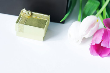A small gift box of gold color, a brown gift bag and white and pink tulips on a white background. Gift for Valentine's Day.