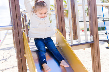 Beautiful toddler child girl wearing jacket playing with slide on the beach