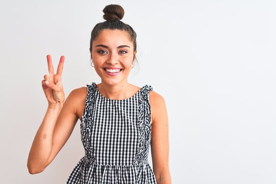 Beautiful woman with bun wearing casual dresss standing over isolated white background showing and pointing up with fingers number two while smiling confident and happy.