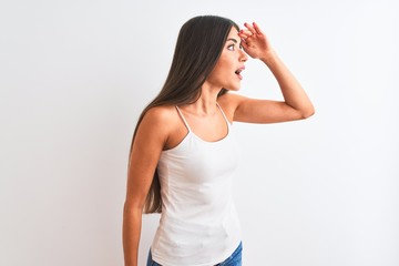 Young beautiful woman wearing casual t-shirt standing over isolated white background very happy and smiling looking far away with hand over head. Searching concept.