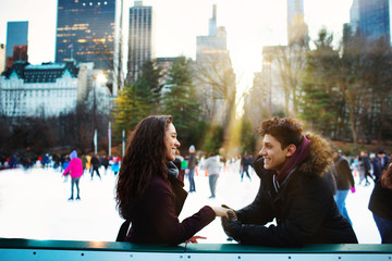 Portrait of a happy young hispanic couple smiling and holding each other while ice skating outside...
