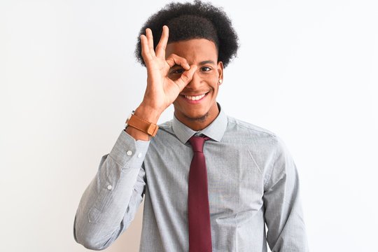 Young african american businessman wearing tie standing over isolated white background doing ok gesture with hand smiling, eye looking through fingers with happy face.