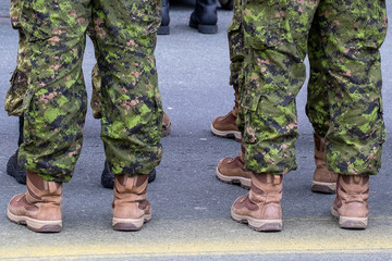 Multiple soldiers stand in camouflage fatigues and tan-colored desert boots. The men are lined up in two rows. The green uniforms are tucked inside high top boots.