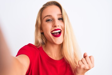 Young beautiful woman wearing t-shirt make selfie by camera over isolated white background screaming proud and celebrating victory and success very excited, cheering emotion