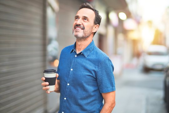 Middle age handsome man standing on the street drinking take away coffee smiling