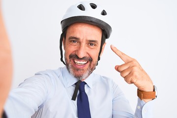 Middle age businessman wearing bike helmet make selfie over isolated white background very happy pointing with hand and finger