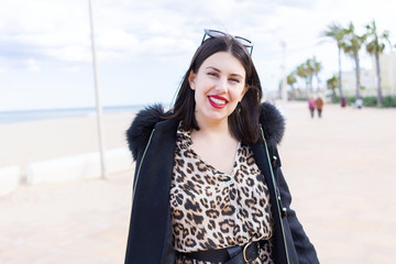 Young beautiful woman wearing sunglasses and coat walking on the promenade