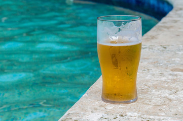 Vaso de cerveza a orilla de piscina. Vaso con cerveza helada. Bebiendo cerveza en orilla de piscina