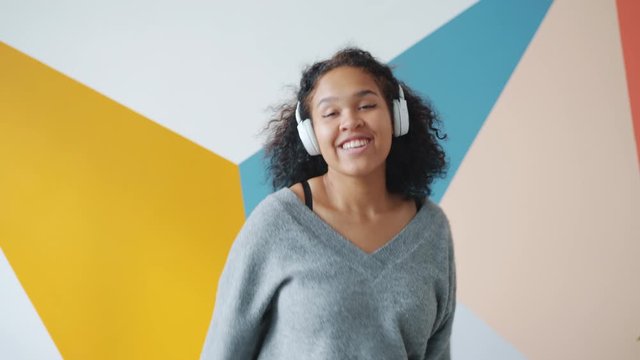 Slow motion of carefree African American lady dancing indoors wearing wireless headphones enjoying modern music. Contemporary lifestyle and joy concept.