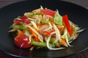 Somtam or Spicy green papaya salad, Thai cuisine. Green  papaya salad is a spicy salad made from shredded unripe papaya. Originating from ethnic Lao people, it is also eaten throughout Southeast Asia.