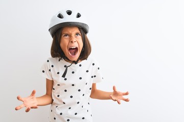 Beautiful child girl wearing security bike helmet standing over isolated white background crazy and mad shouting and yelling with aggressive expression and arms raised. Frustration concept.