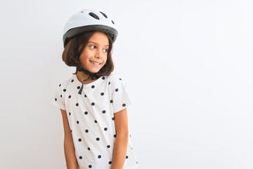 Beautiful child girl wearing security bike helmet standing over isolated white background looking away to side with smile on face, natural expression. Laughing confident.