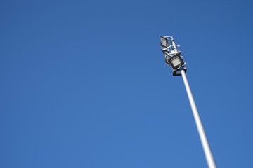A lamp post with LED beam reflectors on empty vast blue sky.