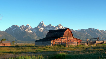 sunrise view of grand teton and a mormon row barn © chris