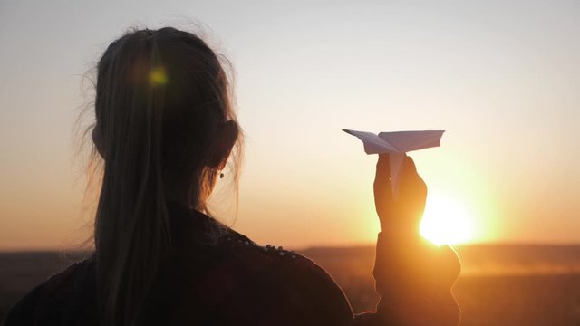 Happy little girl playing with a paper airplane outdoors during sunset. Concept big child dream.