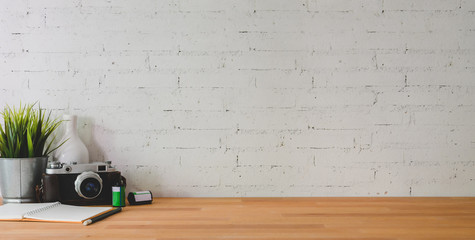 Cropped shot of comfortable workplace with camera and office supplies on wooden table and brick wall