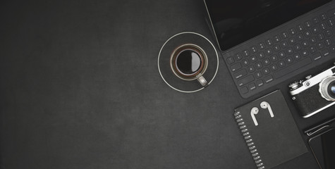 Top view of dark modern workplace with tablet, coffee cup and office supplies on black desk