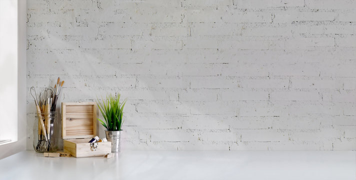 Cropped shot of minimal artist workplace with painting tools on white table and white brick wall
