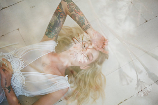 overhead shot of model with tattoos laying on floor, double exposed with flowers