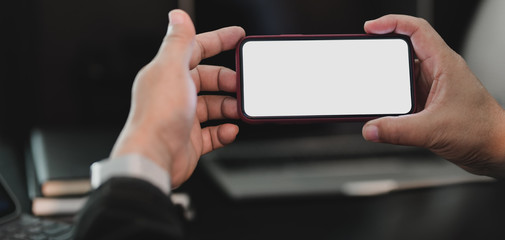 Cropped shot of professional businessman holding blank screen smartphone in dark modern office room