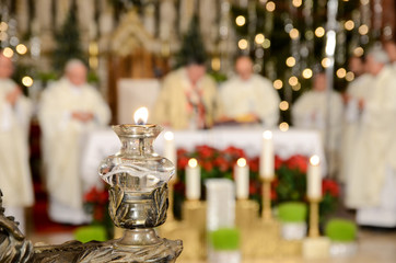 Cardinal and priest in front of the altar in catholic church. Lit candle. Christmas Midnight mass...