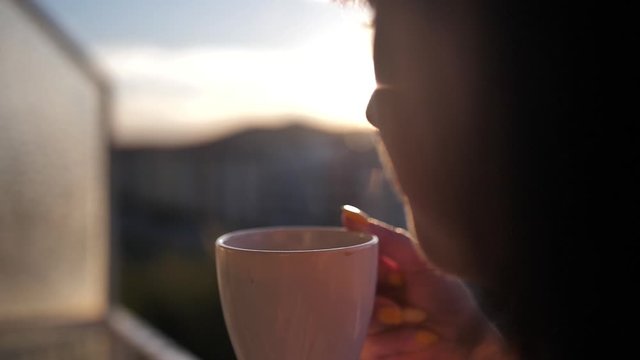 woman drinking coffee on the balcony admiring the sunset, slow motion