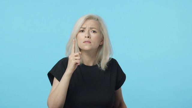 Slow-motion bossy and displeased blond woman shushing you angry, frowing, press finger to lips hush gesture, say shh stop talking, be quiet, demand silence, standing blue background