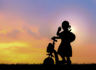 Silhouette of little girl using a scooter in nature sunset