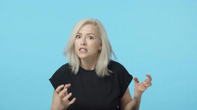 Swear god gonna kill you. Slow-motion aggressive, pissed-off mad blond woman losing temper, clenching hands want strangle someone, squeeze teeth and grimacing angry, standing blue background