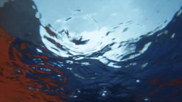 Abstract and hypnotic slow motion shot of raindrops falling into a pool seen from underwater.