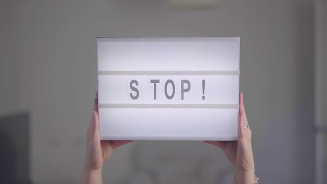 Woman's hands rising a luminous sign with the word "STOP!".