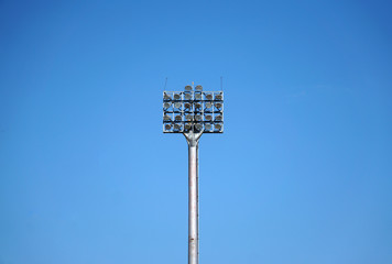                                Spotlights tower with a metal pole for the sports arena. Installed around football stadium. Blue sky background.