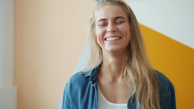 Portrait of joyful young woman with beautiful blond hair laughing on bright background having fun alone wearing casual clothing. People and emotions concept.