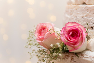 Close up of beautiful white tree tier cake with fresh flowers with fairly light and lanterns glowing in the background. Selective focus. Copy space.
