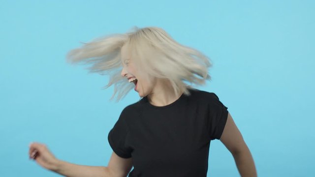 Lets get this party started. Slow-motion carefree upbeat, ecstatic blond woman having fun, whip hair shaking head as dancing wild and joyful, enjoy awesome music festival, triumphing, blue background